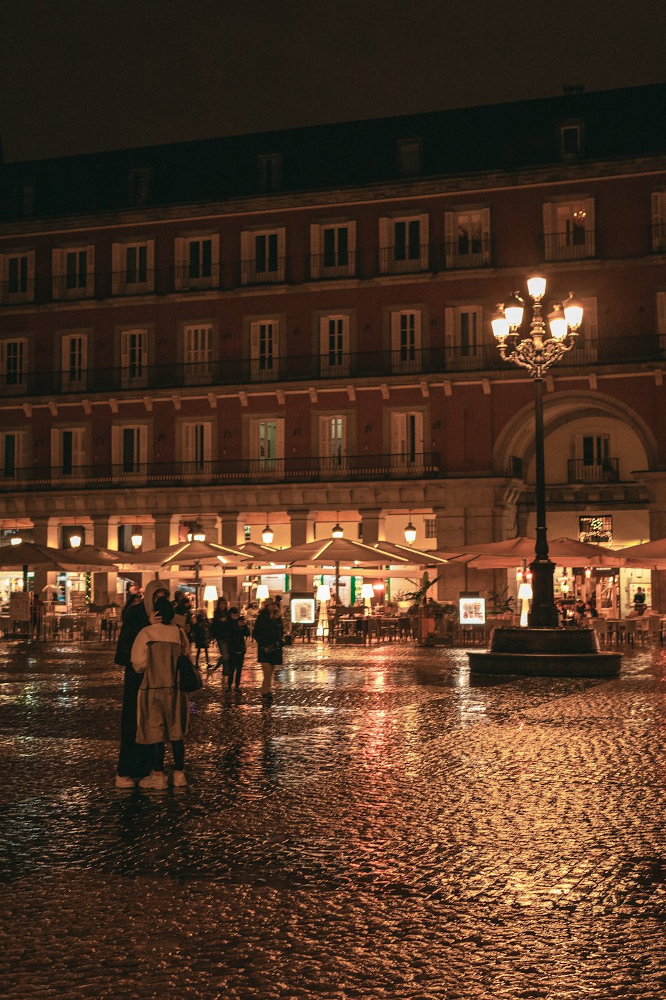 Persone passeggiano in una piazza acciottolata piena di caffè.