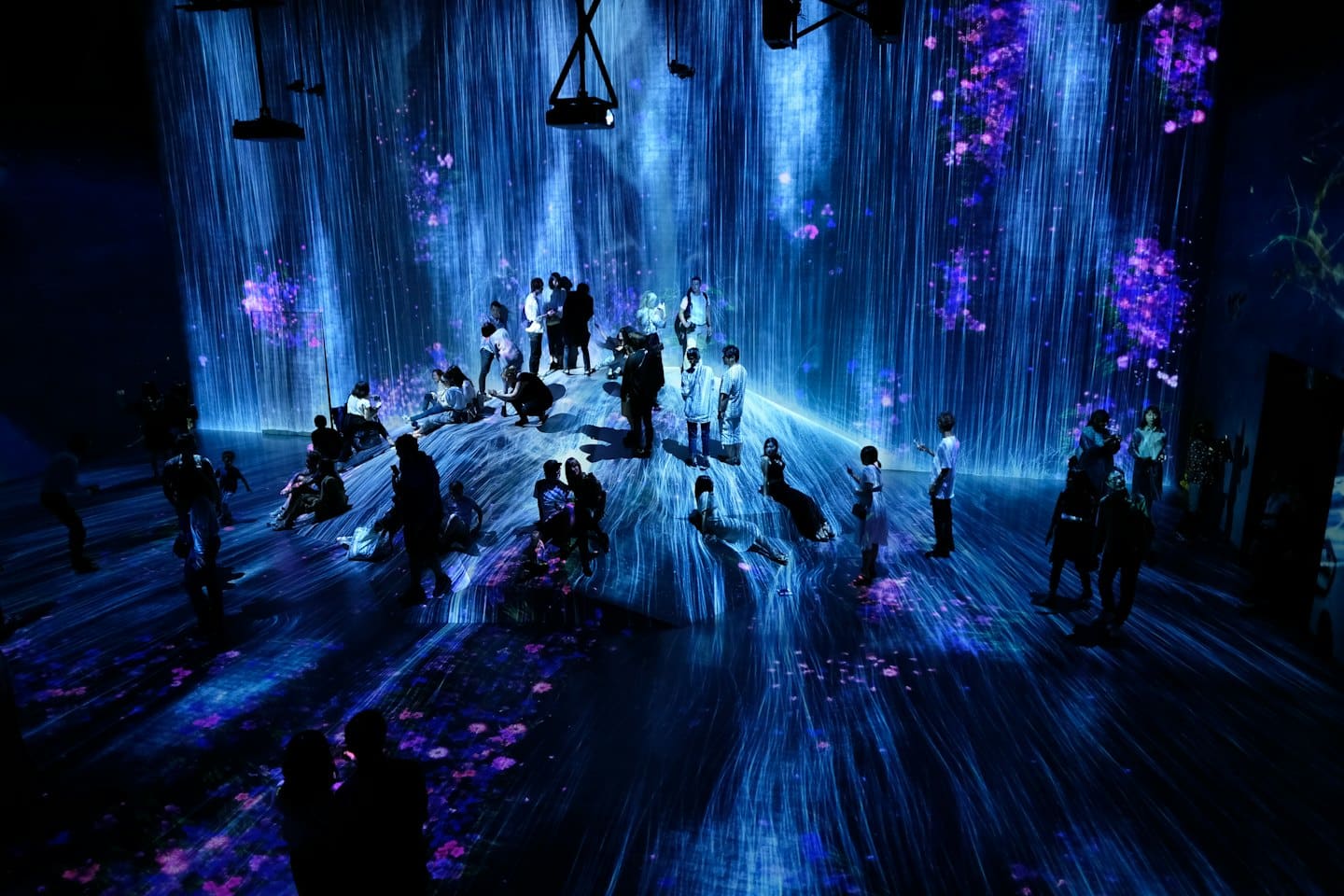 Visitatori passeggiano in una mostra d'arte digitale con proiezioni di cascate.