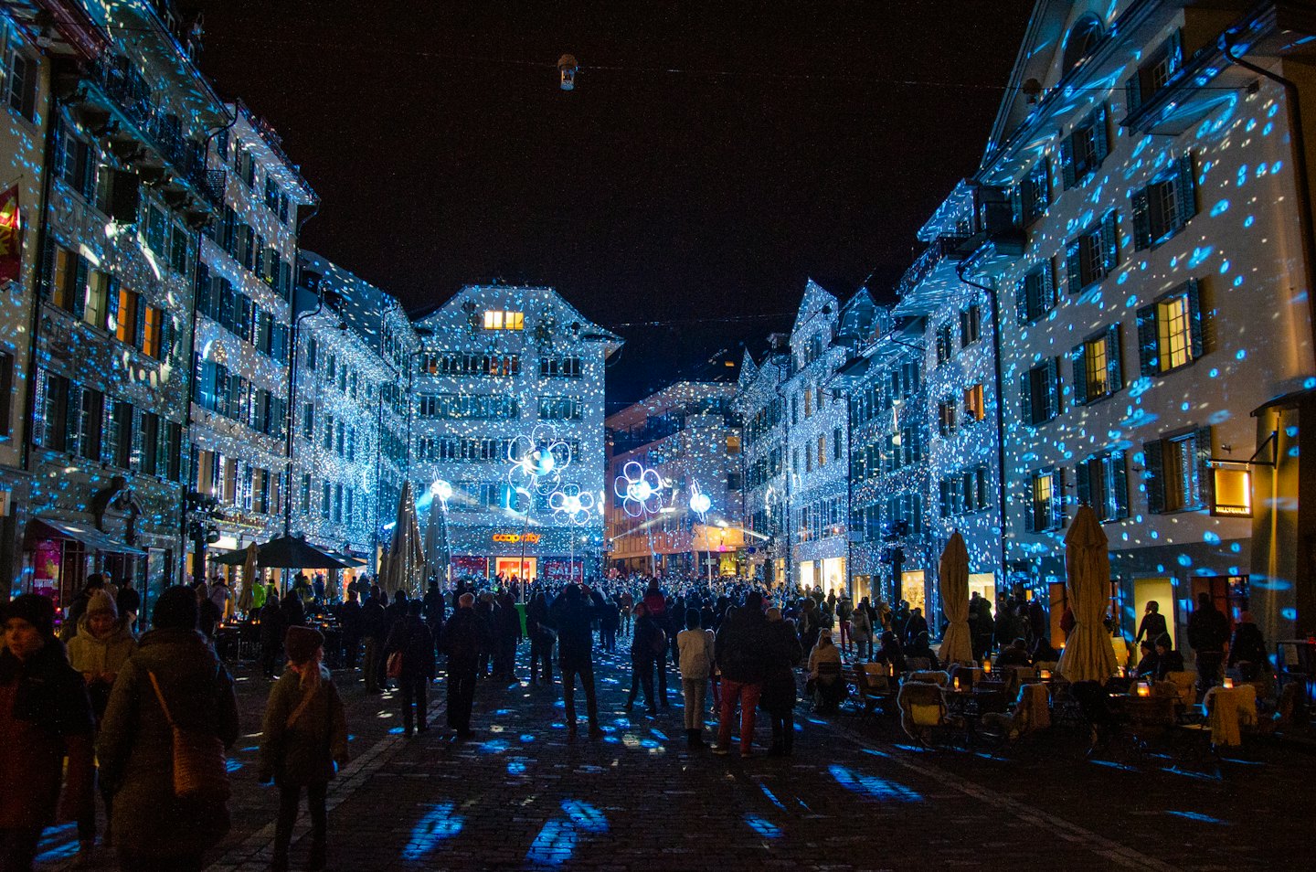 Persone passeggiano in una piazza decorata con luci blu.