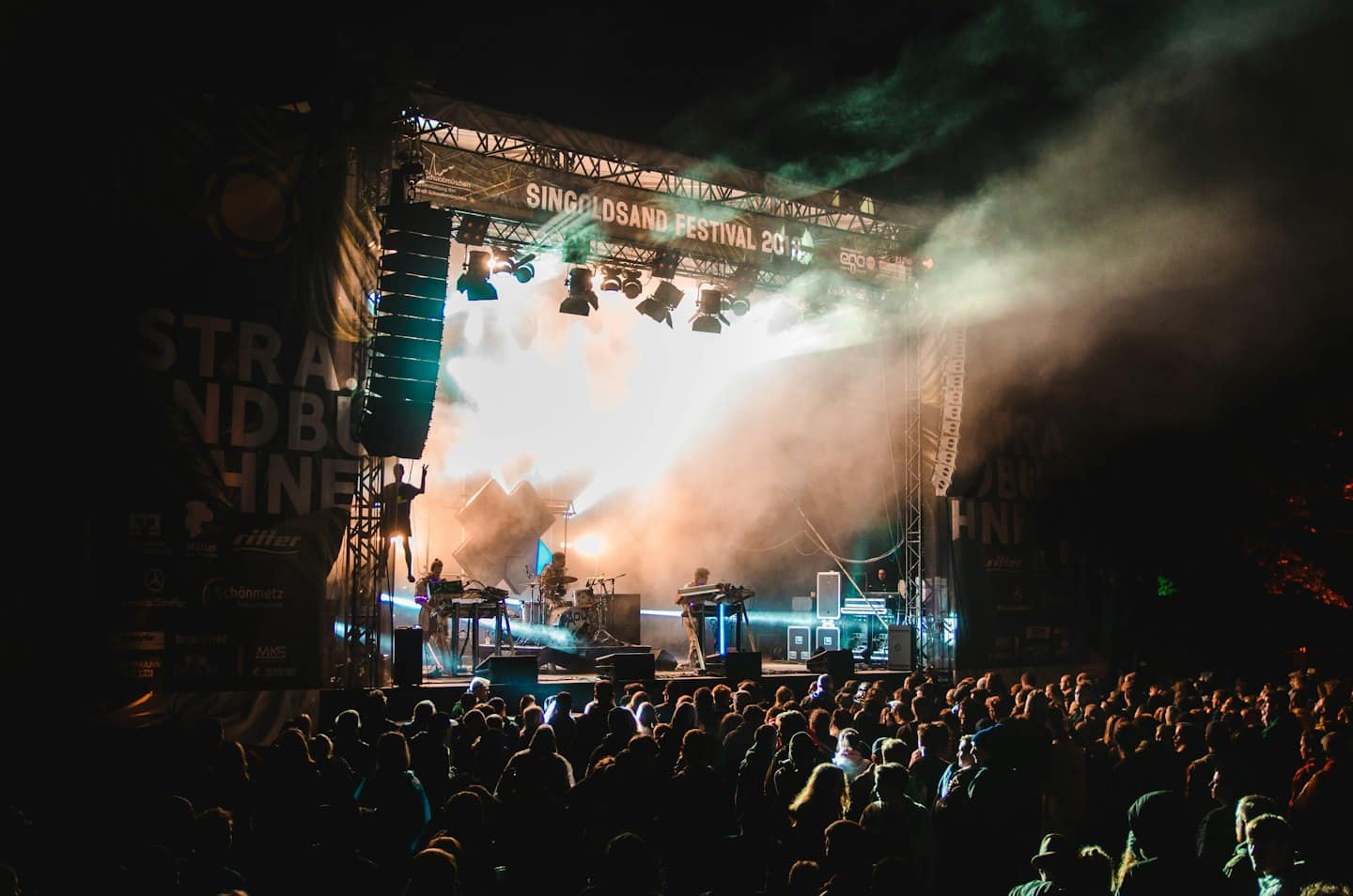 Una band si esibisce su un palco all'aperto sotto luci colorate di notte.