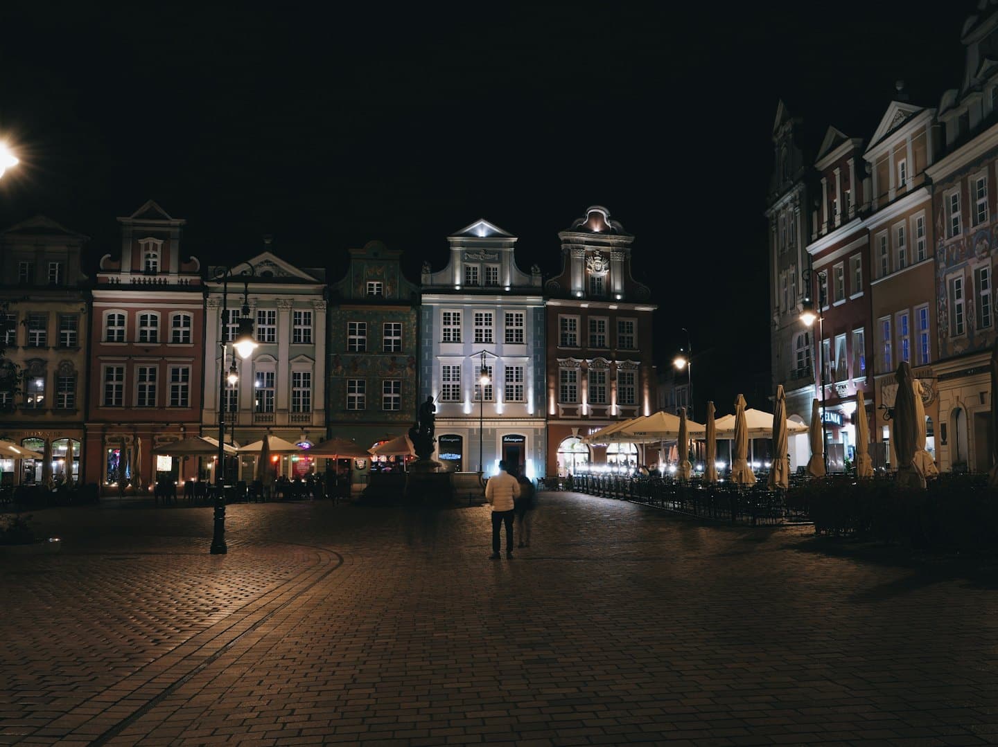 Pedoni attraversano una piazza storica illuminata di notte.